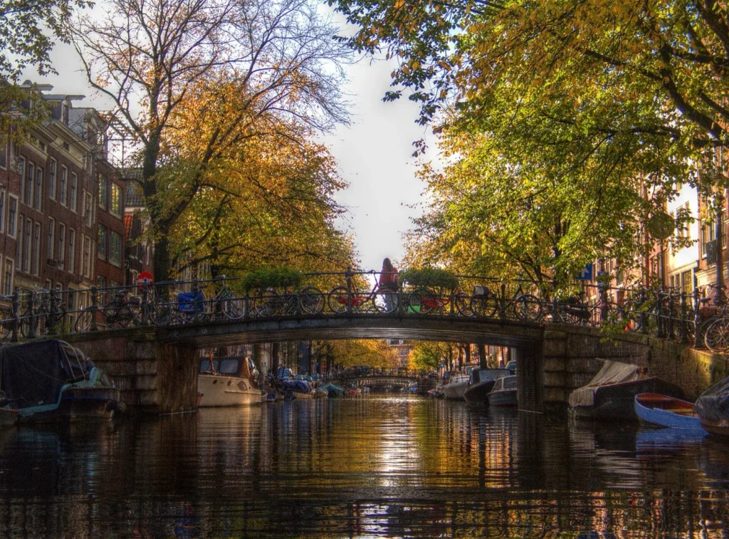 Il ponte Hilletjesbrug sull'Egelantiersgracht, nel quartiere Jordaan, tra alberi autunnali e barche ormeggiate; sullo sfondo un altro ponte