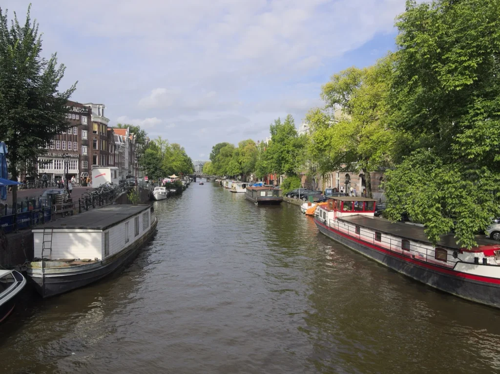 Il canale Prinsengracht visto dal Leliegracht, con case galleggianti ormeggiate lungo le sponde alberate