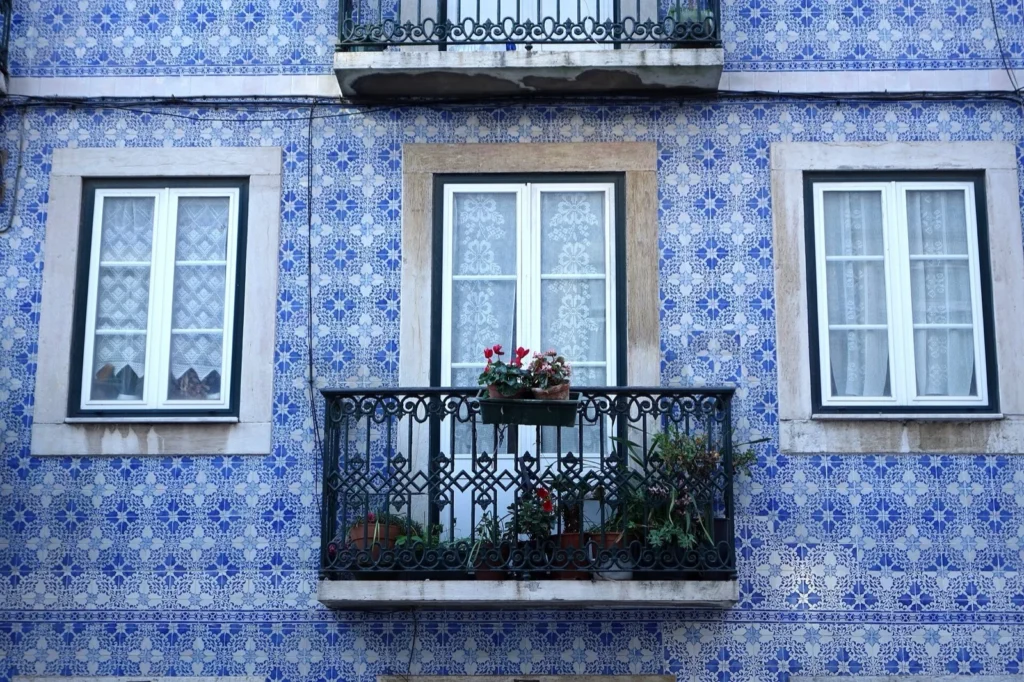 Facciata di un edificio di Lisbona rivestita di azulejos bianchi e blu, con finestre e un balcone in ferro con piante