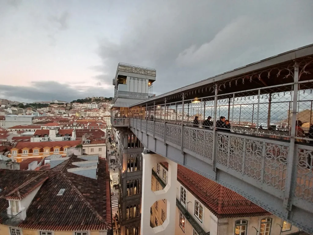 La torre in ferro dell'Elevador de Santa Justa e la sua passerella decorata sopra i tetti di Lisbona, al crepuscolo