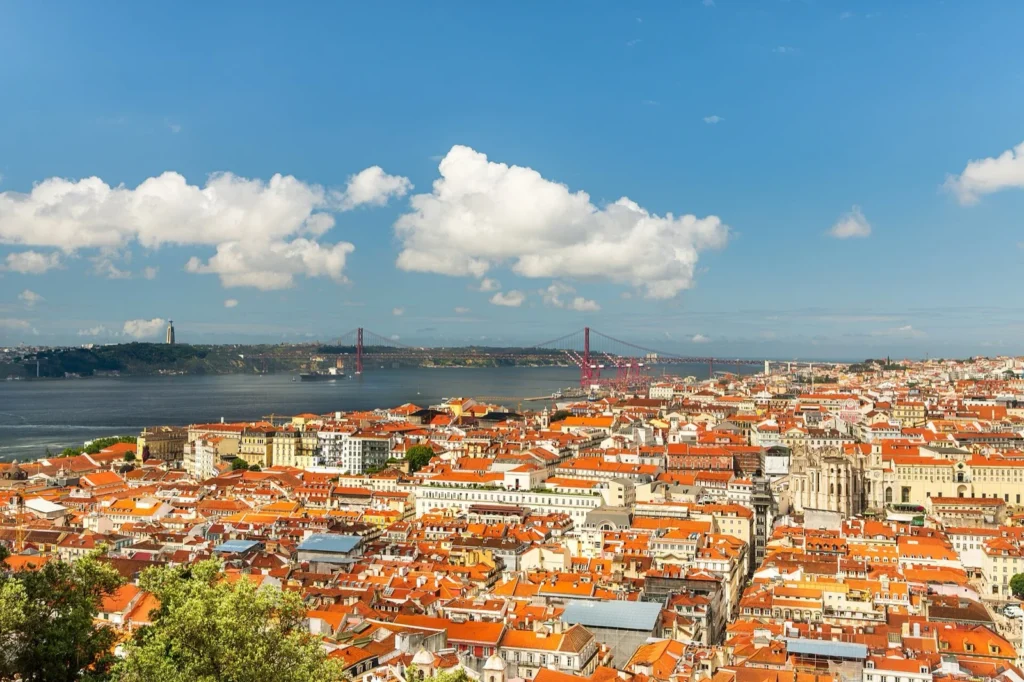 Panorama di Lisbona dal Castelo de São Jorge: i tetti rossi della città e il fiume Tago sotto un cielo azzurro con nuvole