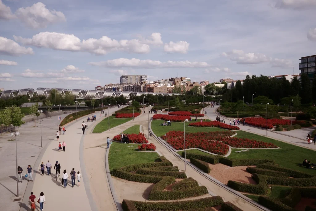 I giardini di Madrid Río con aiuole di fiori rossi, viali pedonali e una passerella sullo sfondo