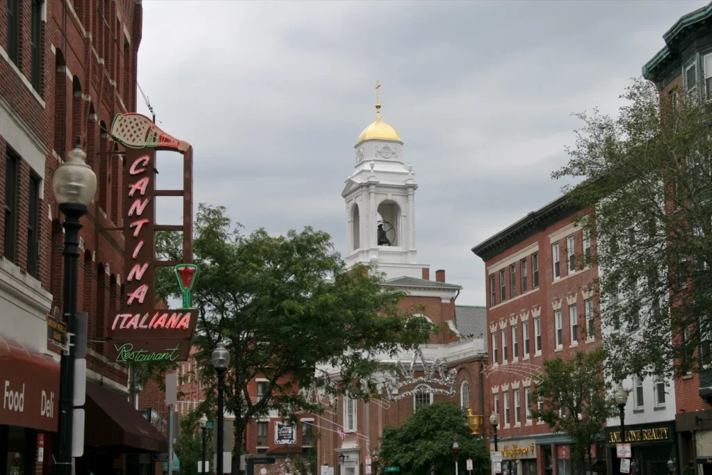 Hanover Street nel North End di Boston, con l'insegna Cantina Italiana, le luminarie sopra la strada e un campanile bianco con la cupola dorata