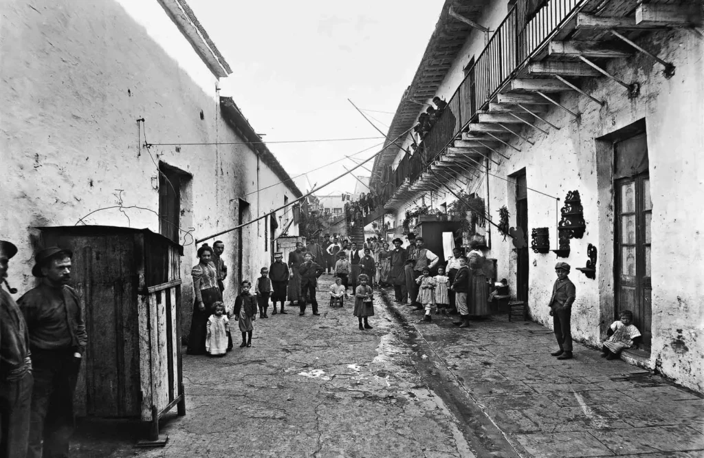 Il lungo cortile di un conventillo di Buenos Aires: muri imbiancati, un ballatoio di legno al piano superiore, fili per i panni e adulti e bambini in posa