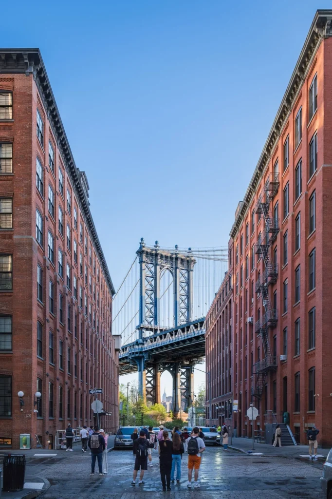 Washington Street a DUMBO, Brooklyn: la strada lastricata tra edifici industriali in mattoni, con il Manhattan Bridge e l'Empire State Building sotto l'arco del pilone