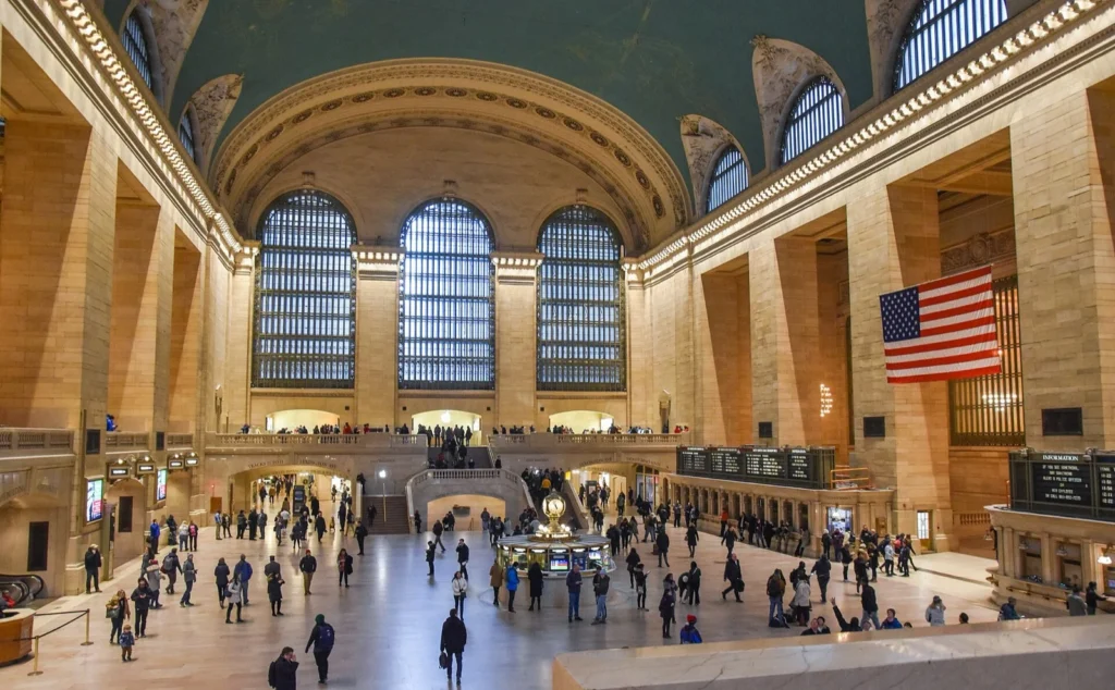 L'atrio principale del Grand Central Terminal visto dall'alto, con le grandi finestre ad arco, la bandiera americana e i passanti