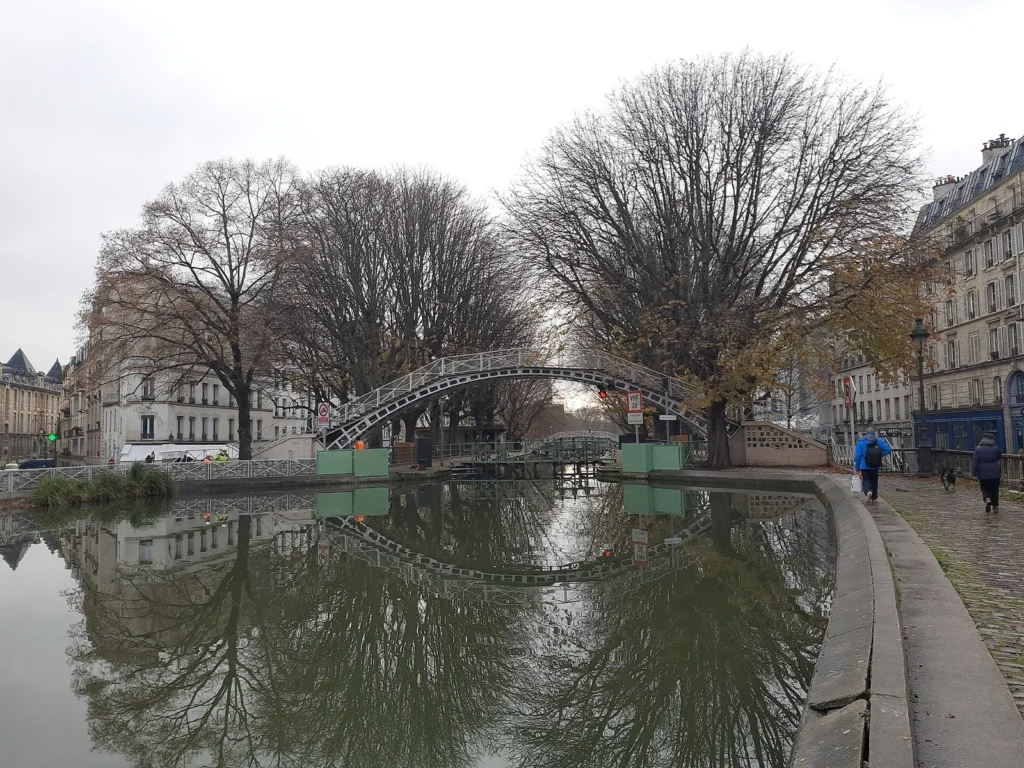 Il Canal Saint-Martin con una passerella in ferro e gli alberi spogli riflessi nell’acqua